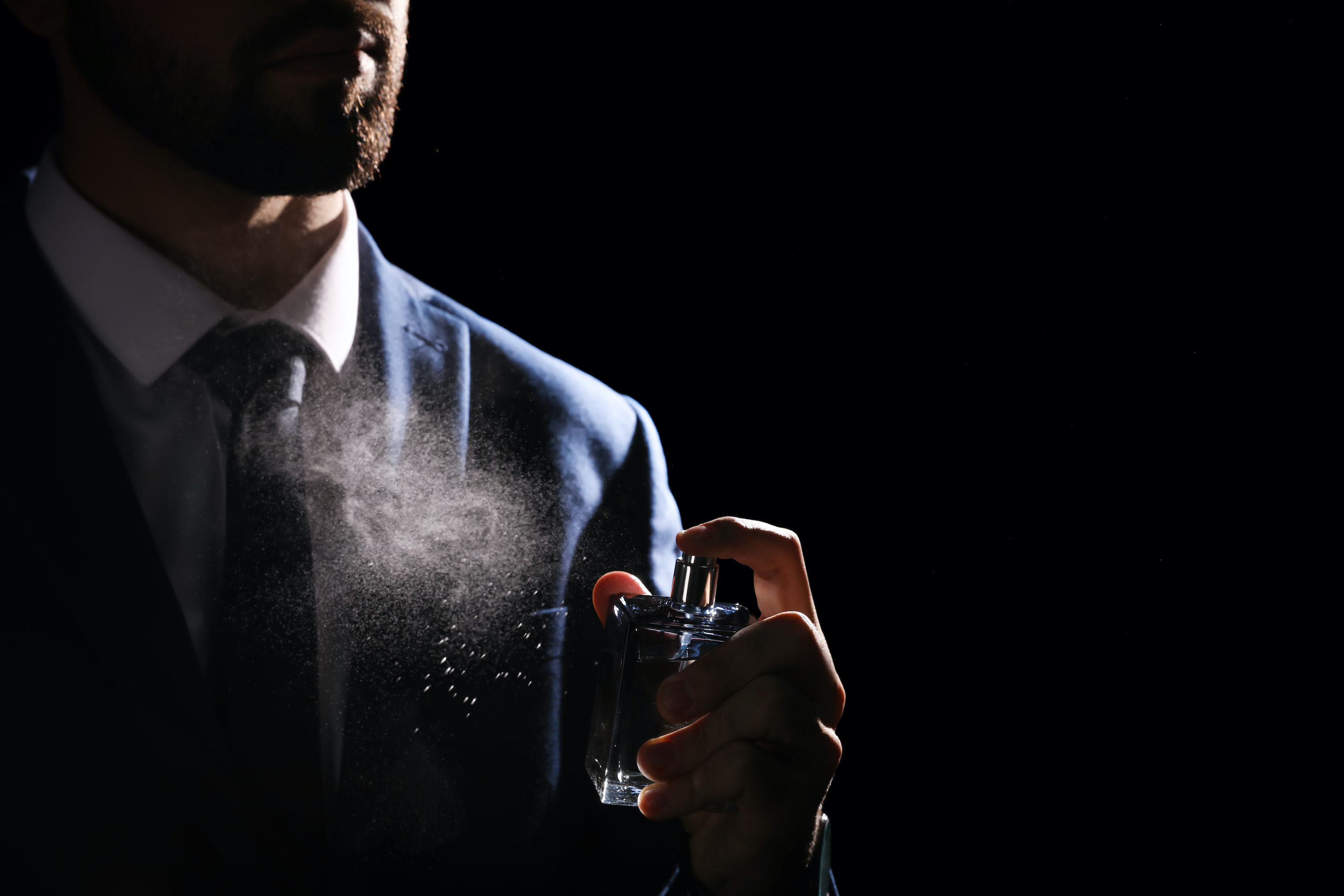 Man spraying luxury perfume on black background, closeup